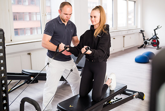 physiotherapeut trainiert frau am fitnessgeraet