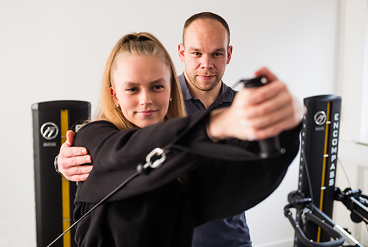 Physiotherapeut trainiert mit einer Patientin am Fitnessgerät